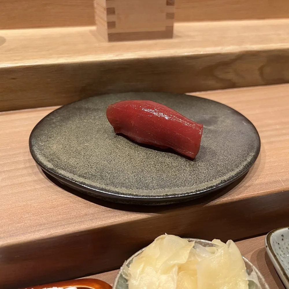 檜木吧台上，深色盤子裡的一貫鮪魚赤身握壽司